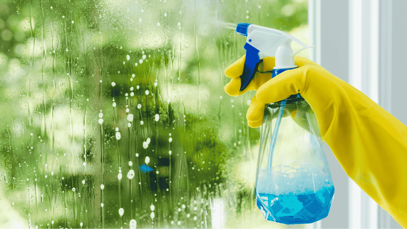 Reinigungskraft sprüht das Fenster mit einem Glasreiniger ein.